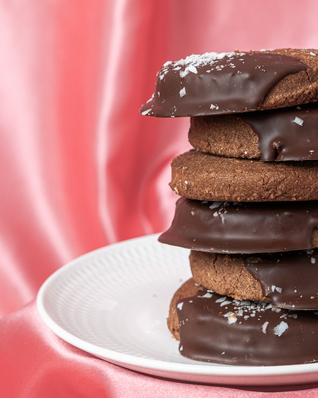 Stack of chocolate-dipped cookies on a white plate with a pink background