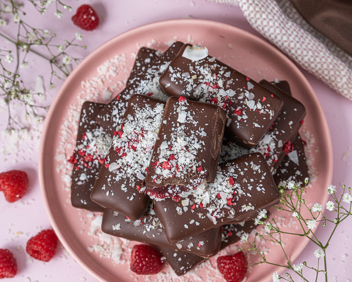 Chocolate treats on a pink plate with raspberries and flowers on a light background