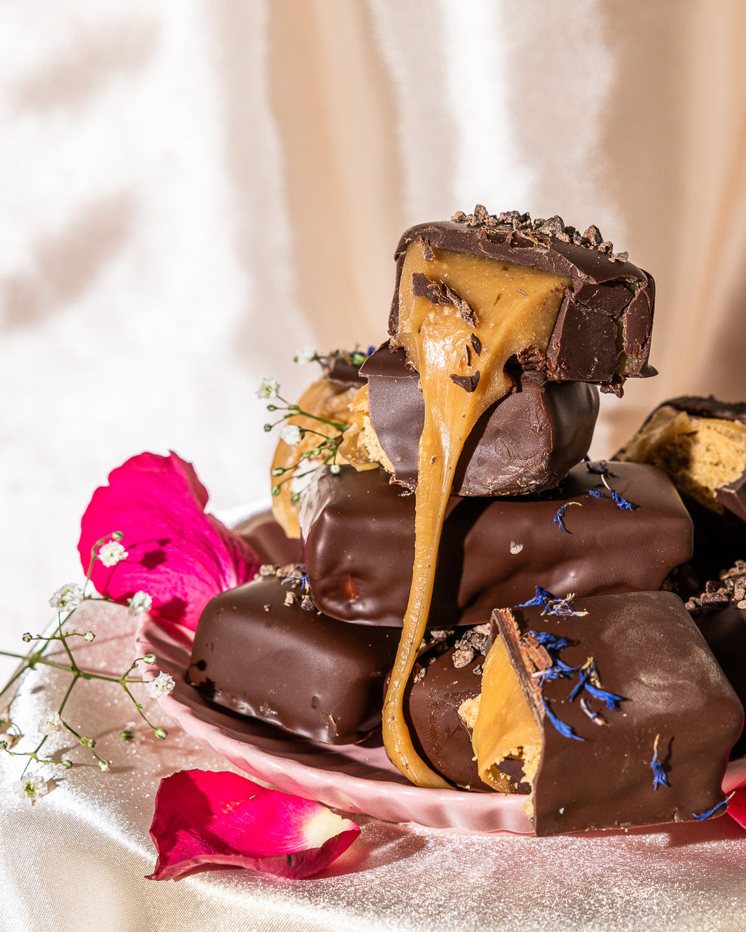 Chocolate-covered treats with a gooey center on a plate with pink petals and greenery.